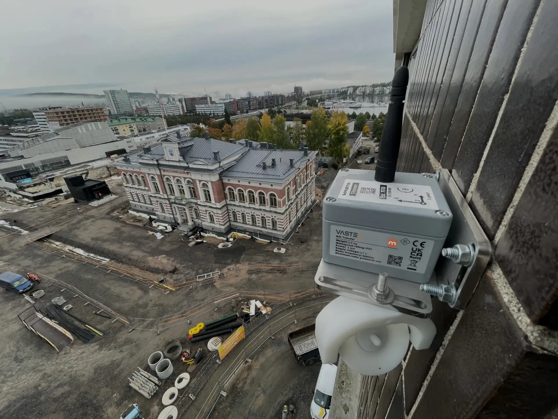 VASTE:n kallistusanturi kiinnitettynä rakennuksen julkisivuun. Alapuolella näkyy työmaa, Kunnallistalo ja Jyväskylän keskusta.